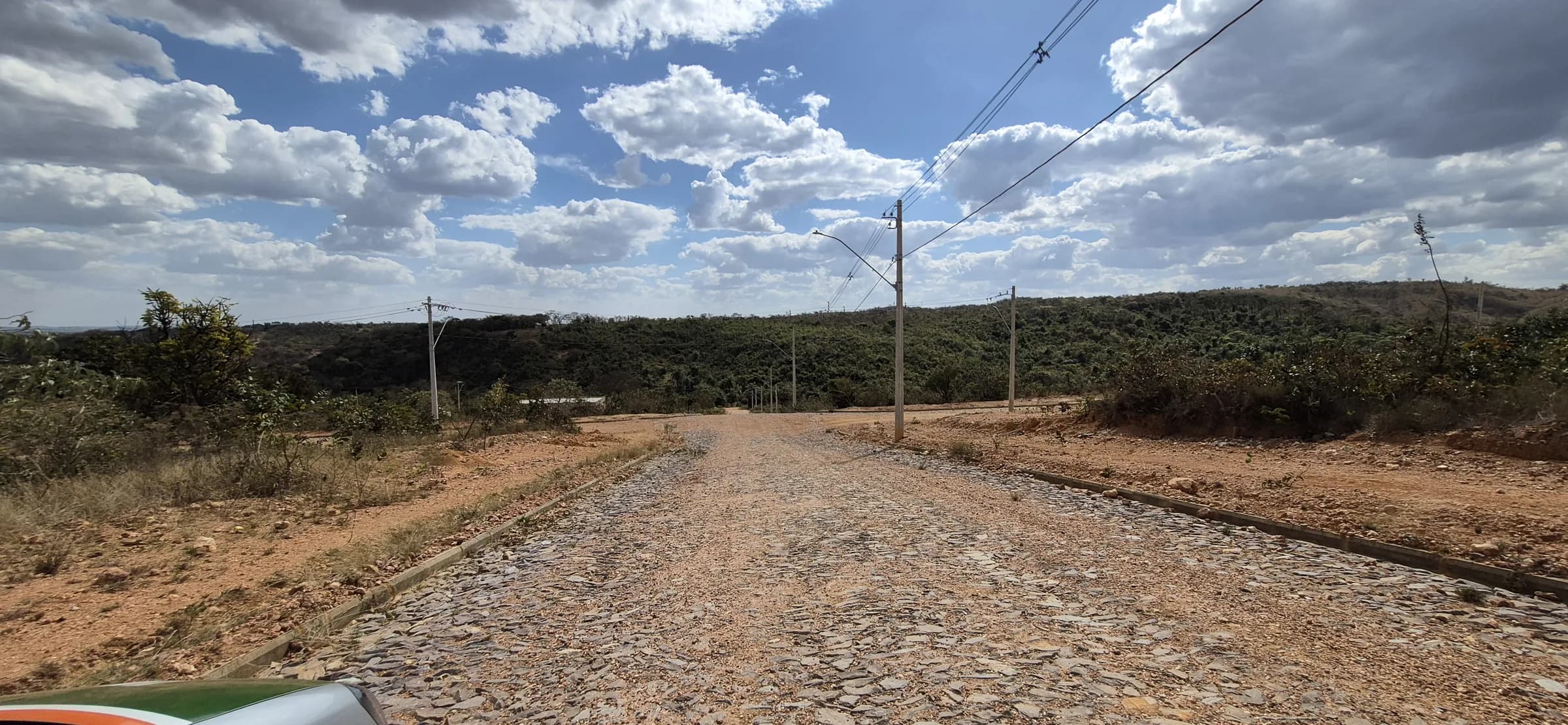 Rua com calçamento de pedra no Mirante da Serra, com postes de energia e vegetação nativa ao fundo
